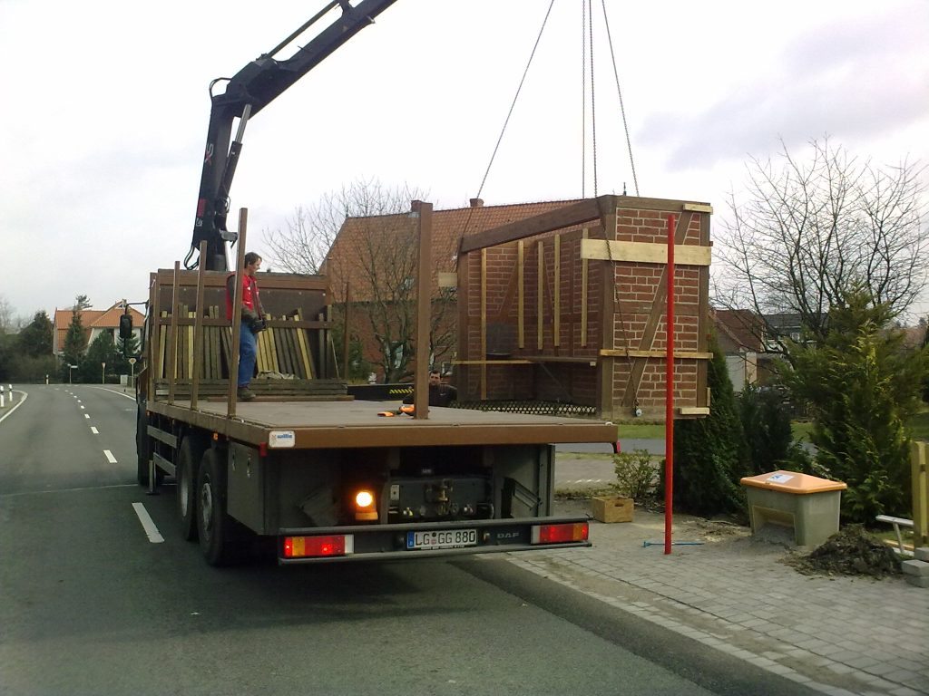 Lkw-Kran hebt Holzhaus auf Bürgersteig
